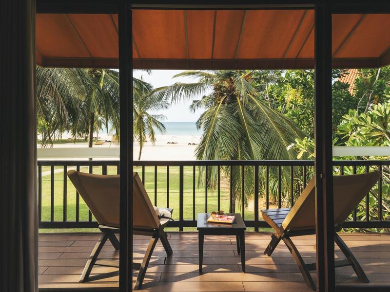 Balcon avec vue sur les palmiers et la plage, deux chaises longues et une petite table.
