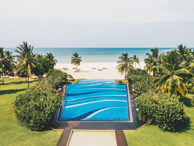 Piscine à débordement avec vue sur la plage de sable blanc et la mer bleue, entourée de palmiers.