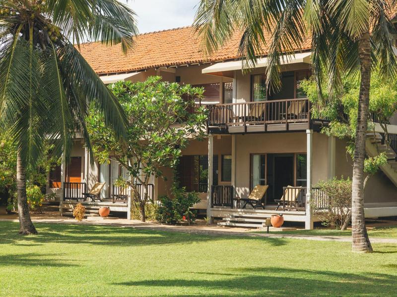 Bâtiment d'hôtel avec vérandas couvertes et palmiers sur une pelouse bien entretenue