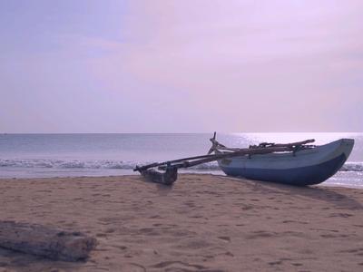 Malá loď leží na písčité pláži s klidným mořem a bledou oblohou v pozadí.