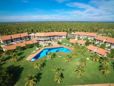 Ośrodek hotelowy z dużym basenem i palmami na rozległym zielonym trawniku.