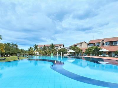 Duży hotelowy basen z niebieskimi kafelkami obok dwupiętrowego budynku hotelowego pod pochmurnym niebem