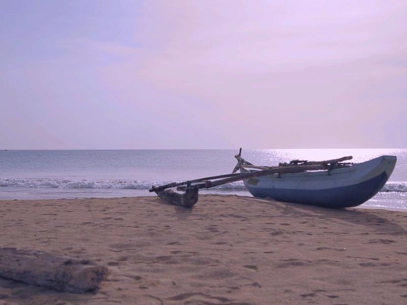 Tradycyjna mała łódź rybacka na spokojnej piaszczystej plaży o wschodzie słońca.