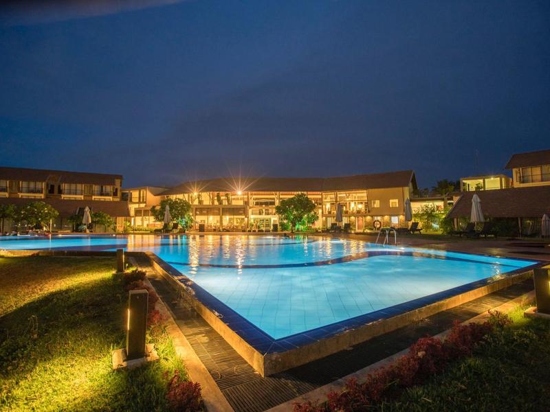 Oświetlony hotelowy basen nocą z otaczającymi budynkami i ogrodem