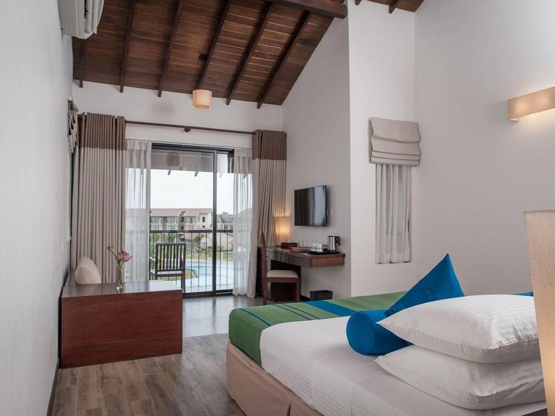 Prosty pokój hotelowy z podwójnym łóżkiem, zielono-niebieską pościelą i balkonem z widokiem na wodę.