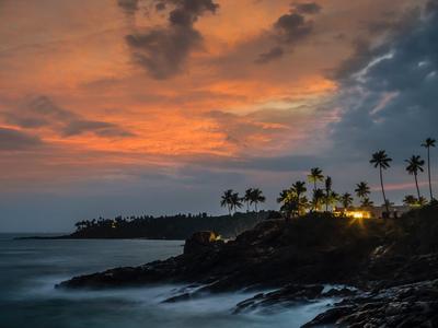 Sonnenuntergang über einer felsigen Küste mit Palmen und sanften Wellen