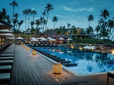 Luxuriöser Poolbereich mit Liegestühlen und Laternen bei Sonnenuntergang in tropischem Resort.