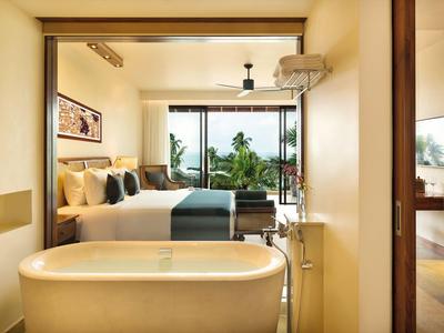 Moderner Hotelbadezimmer mit freistehender Badewanne und Blick auf das Schlafzimmer und den Balkon mit grüner Aussicht.