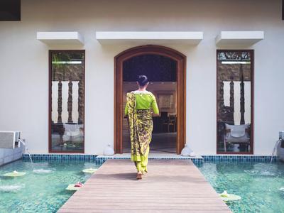 Eine Person in gelbem Kleid läuft über einen Steg zum Eingang eines Gebäudes neben einem Pool.