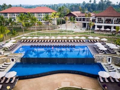 Hotelpool mit Liegestühlen und tropischen Villen im Hintergrund unter blauem Himmel.