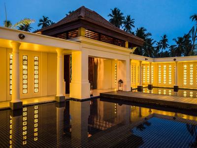 Warm beleuchtetes Hotelgebäude mit Wasserbecken und Palmen bei Dämmerung.