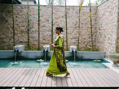 Eine Frau in traditioneller Kleidung geht an einem Wasserbecken vor einer Steinwand entlang.