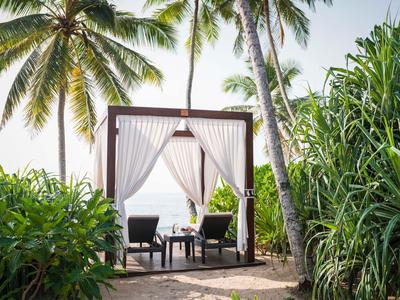 Gemütliche Sitzecke mit Vorhängen unter Palmen am Strand.