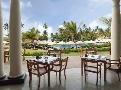 Freiluftrestaurant mit Holztischen und Stühlen, Blick auf einen Pool und Palmen.