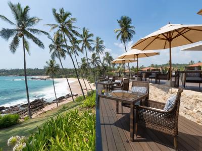 Terrasse eines Hotels mit Stühlen, Sonnenschirmen und Blick auf Palmen und Meer