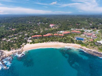 Luftaufnahme eines Resorts an einem tropischen Strand mit klarem blauem Wasser und grüner Umgebung.
