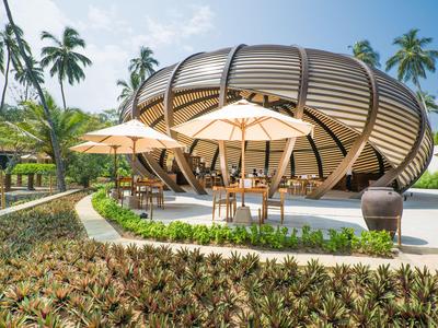 Moderne runde Außenlounge mit Sonnenschirmen und Pflanzen in einem tropischen Hotelresort.