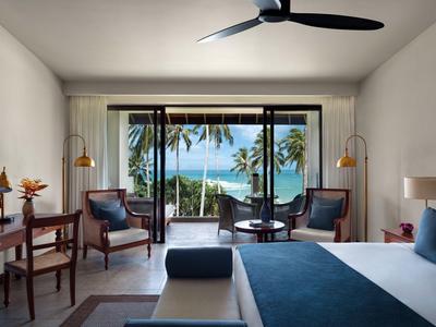 Helle Hotelzimmer mit Balkon und Blick auf das Meer und Palmen.