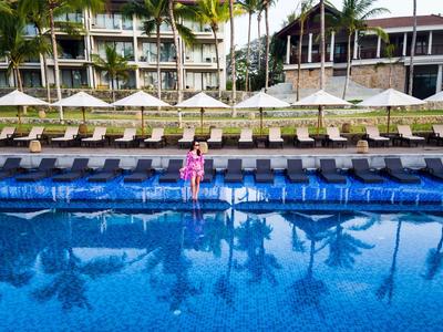 Schwimmbad mit blauer Wasserfläche, Liegestühlen und Hotelgebäude im Hintergrund.