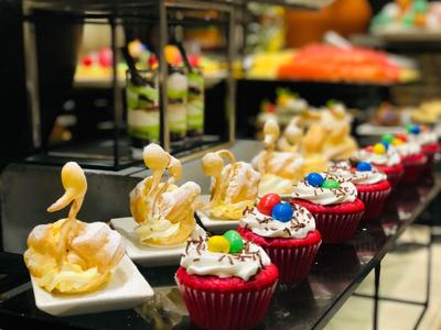 Reihe kleiner, kunstvoll garnierter Desserts in Rot und Weiß auf einem Buffet.