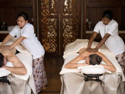 Zwei Masseure massieren gleichzeitig zwei Gäste auf Massageliegen in einem Spa-Raum.