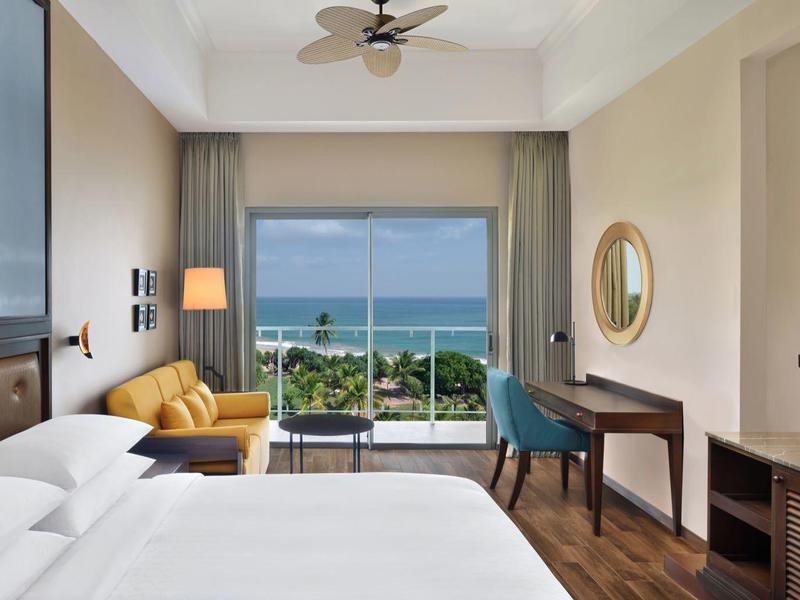 Camera d'albergo con letto matrimoniale, scrivania, TV e balcone con vista mare.