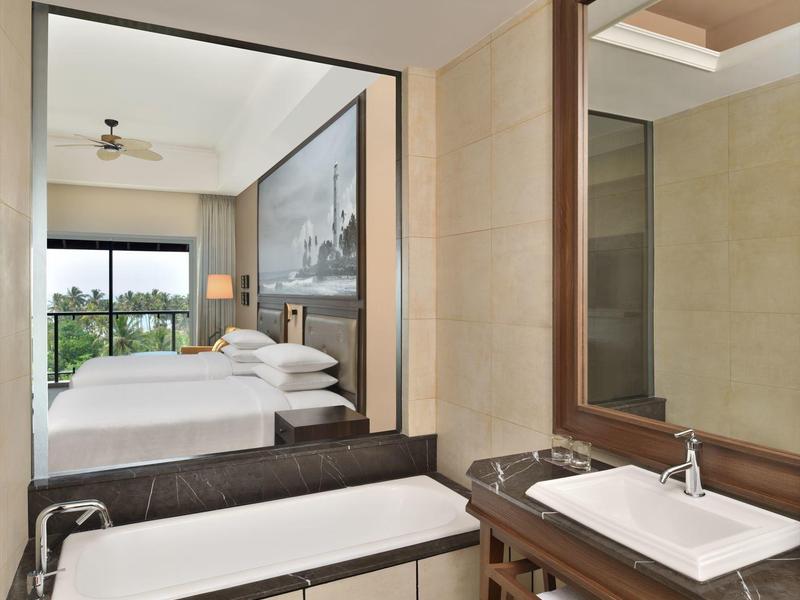 Bagno luminoso con vasca, lavabo, grande specchio e vista sulla camera da letto.