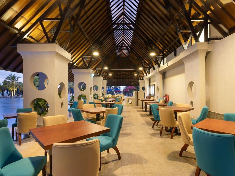 Area pranzo aperta dell'hotel con soffitto a travi di legno e sedie turchesi vicino al lago.