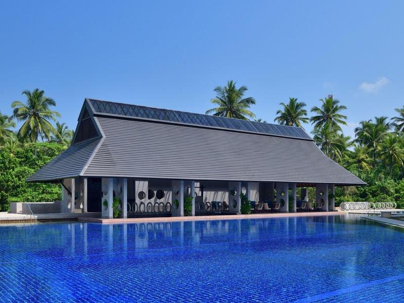 Un padiglione moderno con vista su una grande piscina blu e palme sullo sfondo.