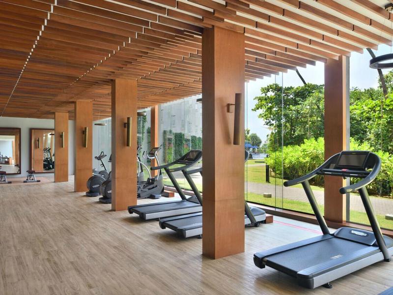 Area fitness coperta con tapis roulant con vista sul giardino verde dell'hotel.