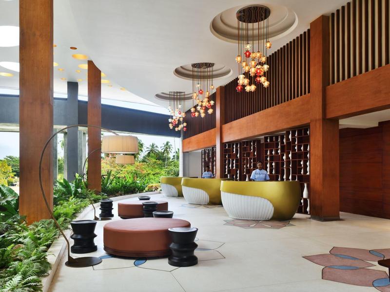 Lobby di hotel moderna con dettagli in legno marrone, sedute eleganti e grandi finestre con vista sul verde.