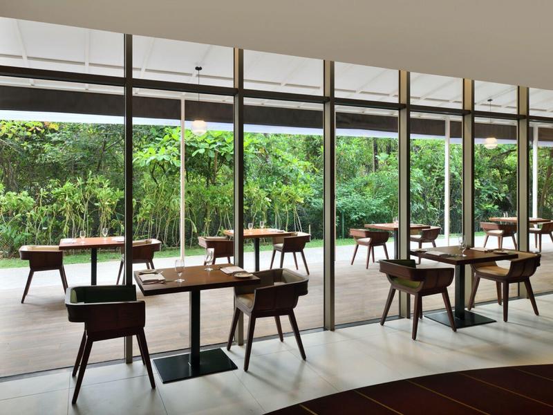 Zona pranzo moderna con tavoli e sedie in legno, grandi finestre con vista su un giardino verde.