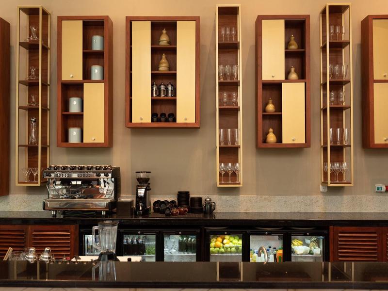 Bar d'hotel moderna con scaffali, frigoriferi per bevande e macchina del caffè su un lungo bancone.