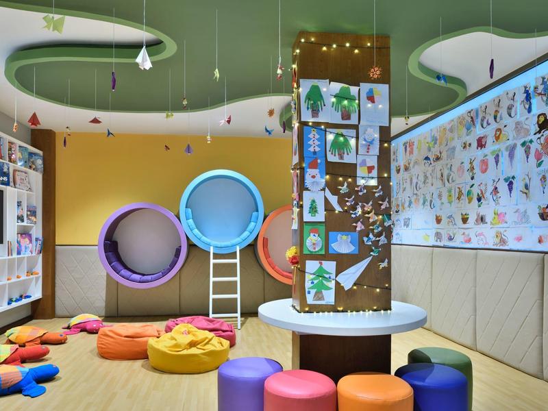 Sala giochi moderna e colorata per bambini con cuscini, giochi da parete e decorazioni luminose.