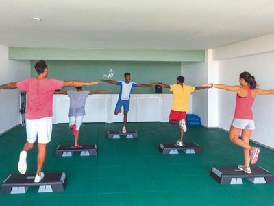 Cinque persone fanno aerobica step in una stanza interna con pavimento verde.