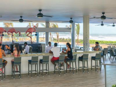 Bar all'aperto con sgabelli alti, clienti seduti e vista su un'area verde.