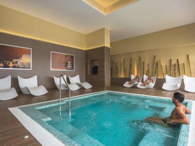 Piscina interna con sedie a sdraio e poltrone, luce soffusa e atmosfera rilassante.