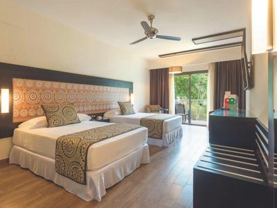 Camera d'hotel luminosa con due grandi letti, pavimento in legno e balcone verde.