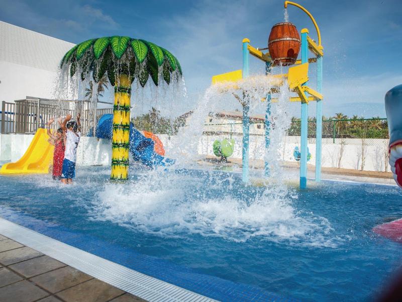 Piscina giochi con scivoli colorati e spruzzi d'acqua sotto un cielo blu.