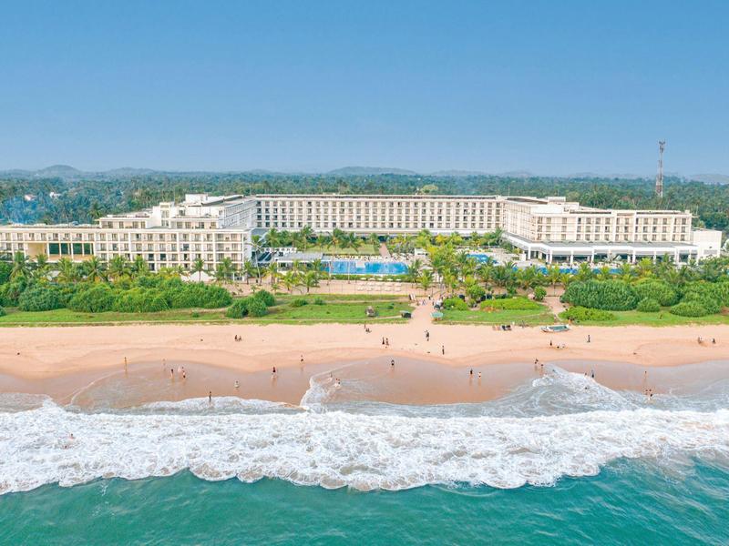 Grande hotel sul mare con spiaggia sabbiosa e piscina all'aperto.
