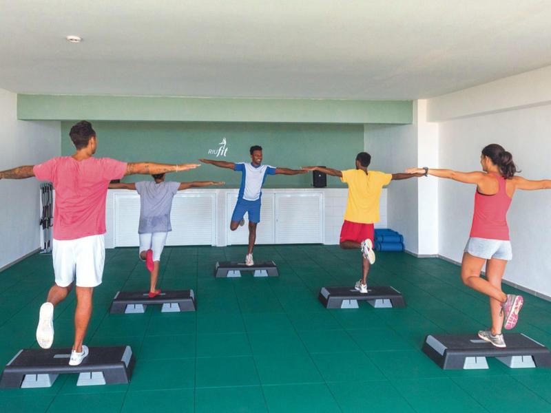 Persone che fanno esercizio su step in una stanza moderna con pavimento verde.