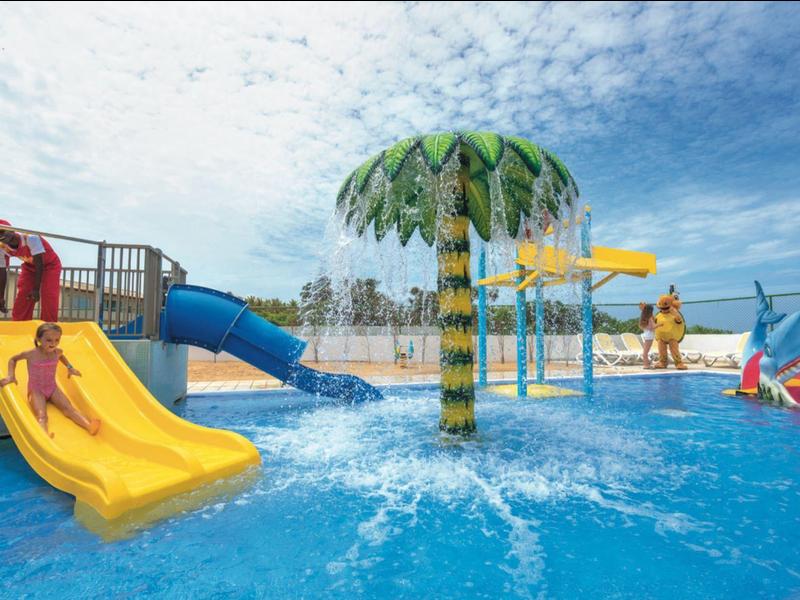 Area giochi acquatica con scivoli colorati e getti d'acqua sotto un cielo parzialmente nuvoloso.