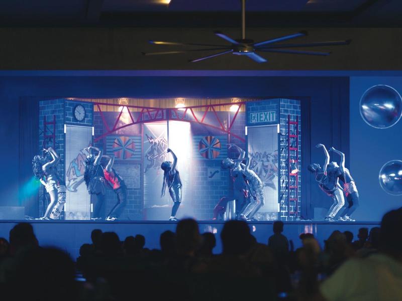 Spettacolo di danza su palco illuminato di blu con pubblico.