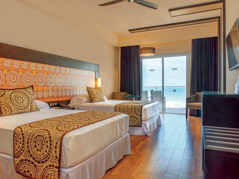 Camera d'albergo luminosa con due letti e vista sul mare dal balcone.