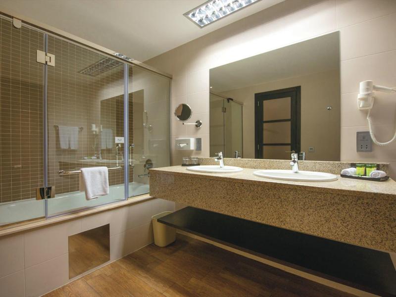 Bagno moderno con doppio lavabo, specchio illuminato e vasca con porta in vetro.