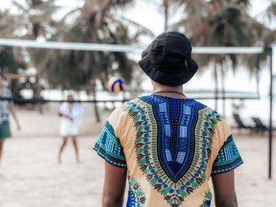 Person mit buntem Hemd und Hut schaut auf Volleyballspiel im Freien
