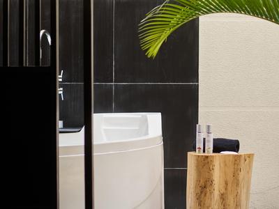 Moderner Badbereich mit freistehender Badewanne, Holzbeistelltisch und tropischer Pflanze.