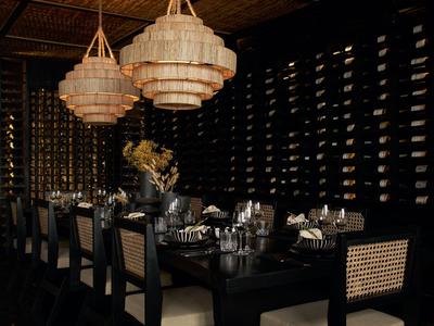 Elegantes, dunkles Restaurant mit Weinwand und großen hängenden Lampen über einem gedeckten Tisch.