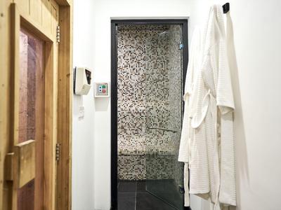 Innenansicht mit zwei weißen Bademänteln an der Wand und einer Glastür mit Muster.