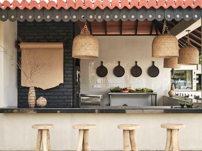 Moderne Outdoor-Küchenzeile mit Holzhockern und Deko-Elementen unter rotem Ziegeldach.